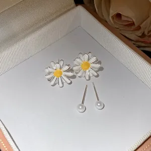 Close-up view of daisy flower and pearl stud earrings set in a cream jewelry box