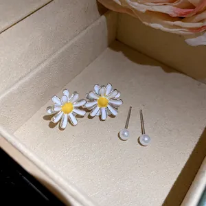 Close-up of elegant white daisy flower and pearl stud earrings set in a beige box.