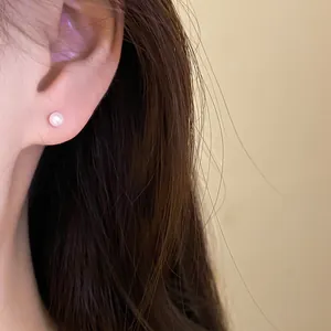 Close-up showing the elegant wearing effect of a small white pearl stud earring.