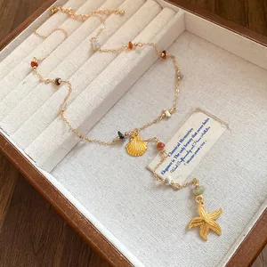 Detail view of gold shell and starfish necklace with colored stones in a wooden tray