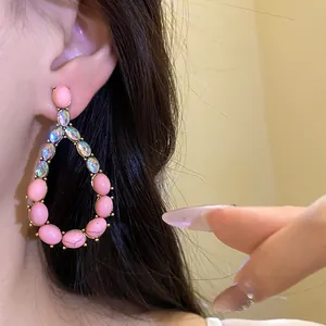 Dettaglio macro di orecchini vintage a goccia con pietre rosa e strass scintillanti indossati