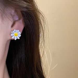 Close-up view of elegant white daisy flower enamel stud earrings being worn on the ear