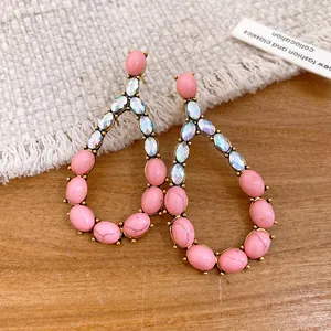 Primo piano di orecchini retrò con pietre rosa e cristalli iridescenti su legno.