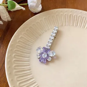 Détail d'une pince à cheveux en zircon avec un ours en résine violette sur une assiette.