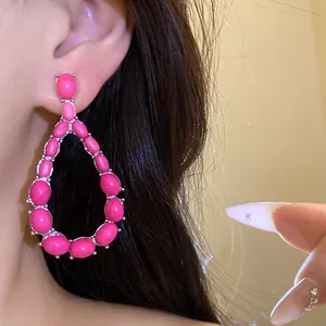 Vista dettagliata di orecchini a goccia in pietra rosa vibrante indossati da una modella di profilo