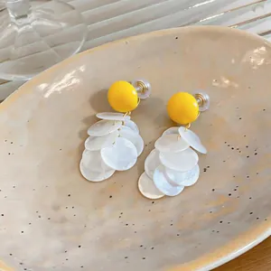Detailansicht gelber Harz-Ohrclips mit mehrlagigen, weißen, muschelartigen Scheiben