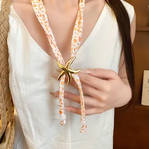 Close-up detail of the gold starfish pendant on a marine-themed printed scarf necklace