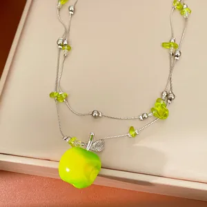 Close-up of double-layered necklace featuring a vibrant green resin apple pendant