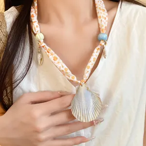 Detail shot of a seaside style silk scarf necklace with a large natural shell pendant.