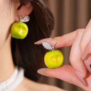 Detailed close-up of bright green resin apple stud earrings with a crystal leaf