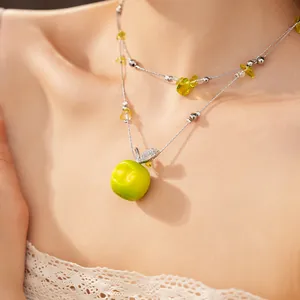 Close-up of double-layered necklace featuring a green resin apple pendant with zircon leaf
