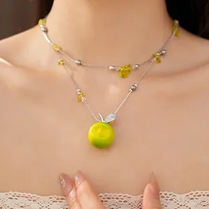 Close-up of double-layer necklace featuring green resin apple and sparkling zircons.