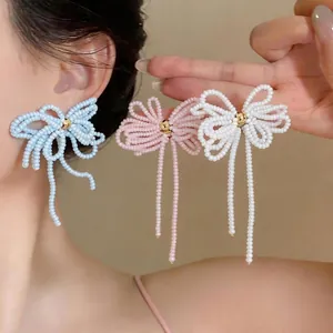 Boucles d'oreilles nœud en perles de verre avec pompons en rose, bleu et blanc.