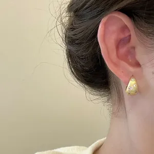 Détail de boucles d'oreilles créoles dorées brossées avec d'élégants zircons étoilés.