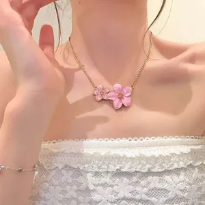 Close-up detail of a pink enamel flower necklace worn by a woman in a white lace top