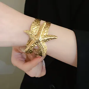 Dettaglio di un bracciale a fascia con stella marina dorata e trama in metallo martellato.