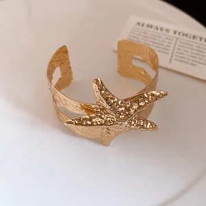 Dettaglio di un bracciale rigido dorato a forma di stella marina con texture martellata