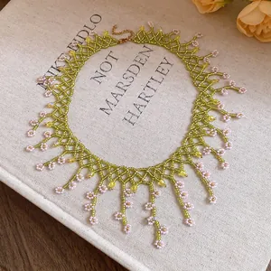 Close-up detail of handmade green beaded necklace with delicate pink floral fringe accents