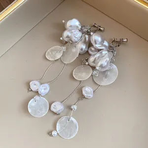 Detalle de pendientes de clip con borlas de perlas barrocas y discos de concha.