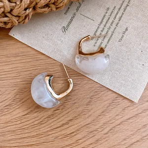 Detail view of retro C-shaped earrings with gold-tone metal and white marble resin finish