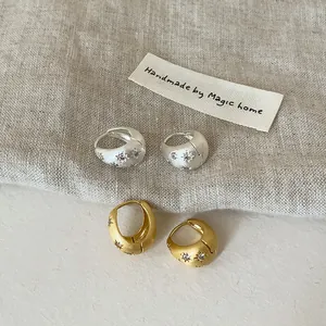 Détail de boucles d'oreilles créoles minimalistes brossées avec motif étoile et zircons