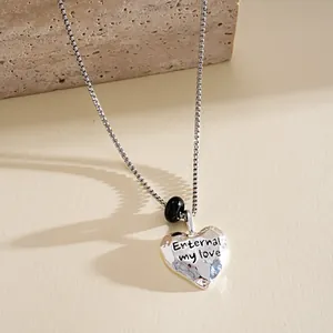 Gros plan d'un collier pendentif cœur argenté avec un message d'amour gravé.