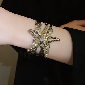 Primo piano di un bracciale rigido aperto a stella marina dorata con trama a pieghe
