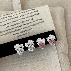 Primo piano di orecchini a lobo con fiori bianchi e cristalli rosa scintillanti.