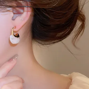 Close-up view of elegant retro C-shaped gold-tone and white resin hoop earrings on model