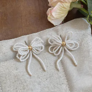 Gros plan d'élégantes boucles d'oreilles nœud en perles de verre blanches fait main.