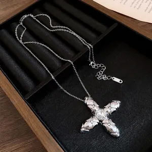 Silver cross pendant necklace with quilted pattern and central crystal on velvet tray