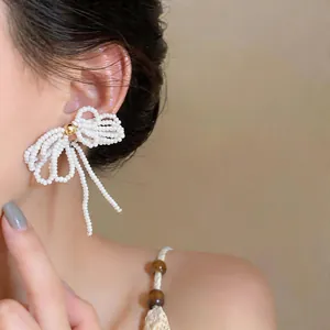 Gros plan de boucles d'oreilles nœud en perles blanches délicates de verre pur.