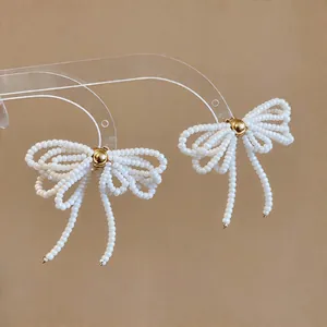 Élégantes boucles d'oreilles nœud en perles de verre blanches avec détail central doré