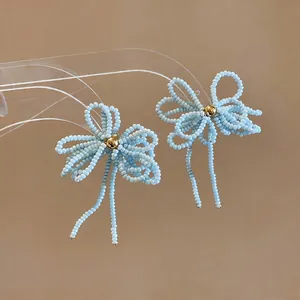 Vue détaillée des boucles d'oreilles nœud en perles de verre bleu clair avec perle dorée centrale.