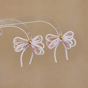 Vue détaillée de boucles d'oreilles nœud en perles roses avec un centre doré élégant.