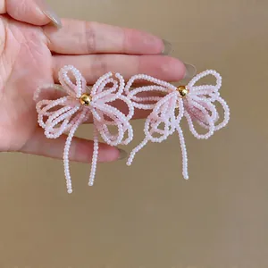 Vue détaillée de boucles d'oreilles en forme de nœud en perles de verre rose pastel.