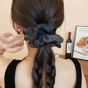Elegant black polka dot fabric scrunchie displayed on a stylish woman's braided ponytail