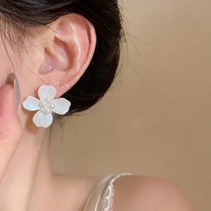 Elegant white four-petal flower pearl stud earrings with silver needles on an Asian model