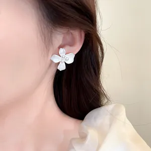 Close-up of elegant white flower earrings with small pearls worn on a model's ear.