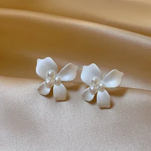 Elegant white flower stud earrings with central pearl accents on luxurious champagne silk fabric