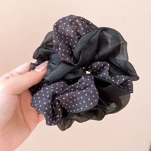 Macro detail view of a black polka dot double-layer scrunchie made of soft chiffon fabric.