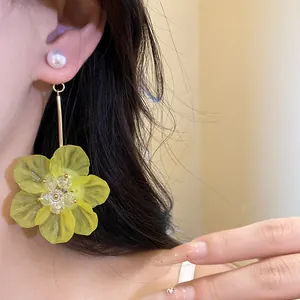 Macro detail of long drop earrings featuring a yellow translucent flower and pearl stud.