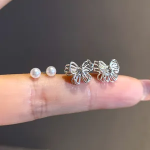 Close-up of silver butterfly and pearl stud earrings displayed on a finger for scale.