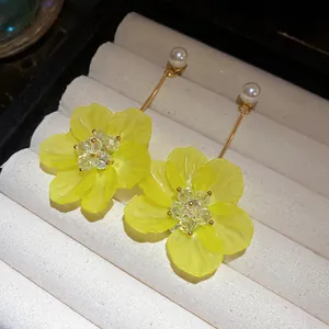 Detailed macro view of yellow matte floral earrings featuring crystal centers and pearls