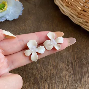 Detailed view of white enamel flower stud earrings with pearl centers held on fingers