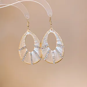 Dettaglio di eleganti orecchini a goccia dorati con avvolgimento in seta e strass.