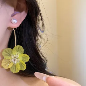 Close-up of elegant yellow flower pendant earrings with a pearl stud on an Asian model.