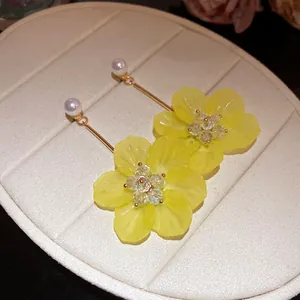 Macro detail of elegant yellow floral pendant earrings with pearl studs and crystal accents.