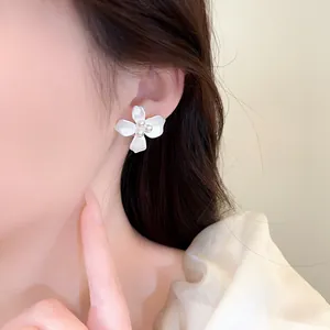 Close-up view of a matte white flower stud earring with delicate pearls worn on an ear.