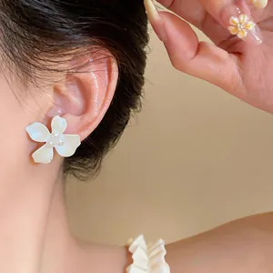 Macro view of a minimalist white enamel flower stud earring with pearl detail worn on the ear